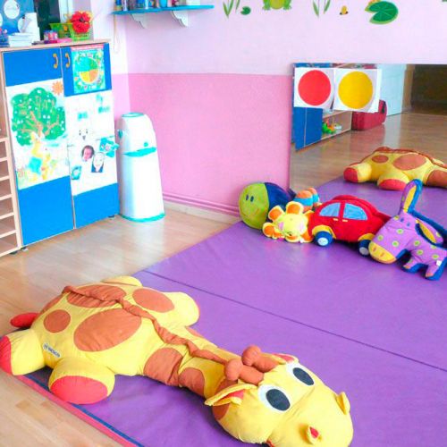 Aula con colchonetas de colores y peluche grande en el suelo