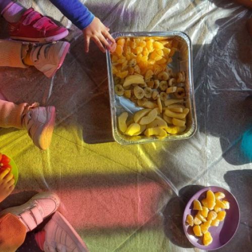 Suelo de patio exterior con niños sentados y recipientes con frutas