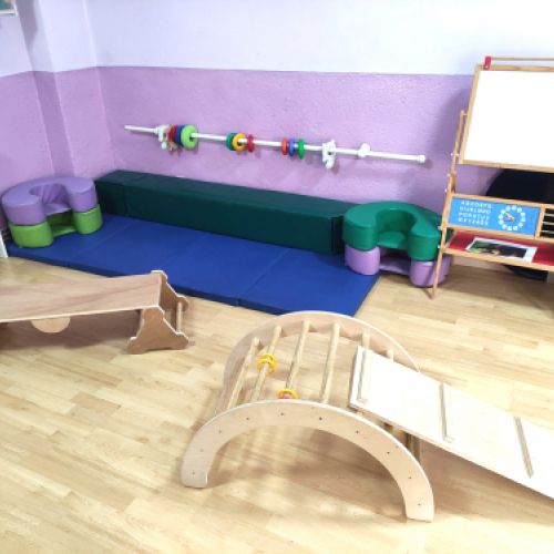 Aula grande con elementos de juego de madera y pizarra blanca al fondo