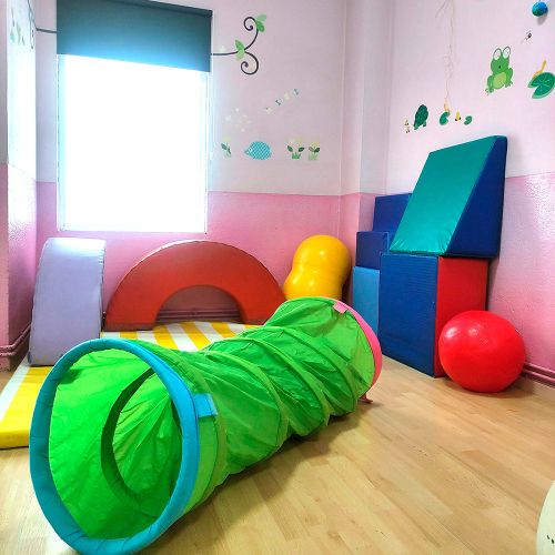 Zona de psicomotricidad con túnel verde y colchonetas de colores