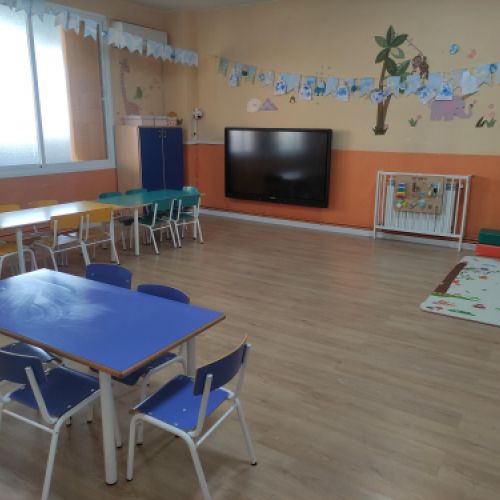 Aula amplia con varias mesas rectangulares con sillas y pantalla grande en pared