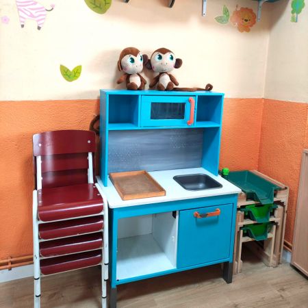 Zona de juegos en aula con cocinita de madera y peluches