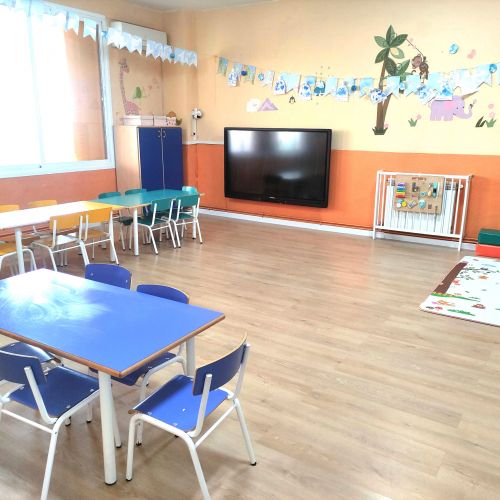 Aula con mesas y sillas azules y pantalla grande en pared del fondo