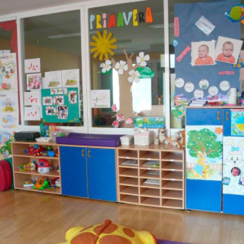 Aula grande con estanterías de madera con juguetes y fotos de bebés en los cristales