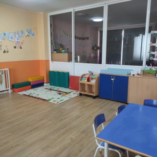 Aula grande con ventanales a la derecha y mesa rectangular azul en primer plano